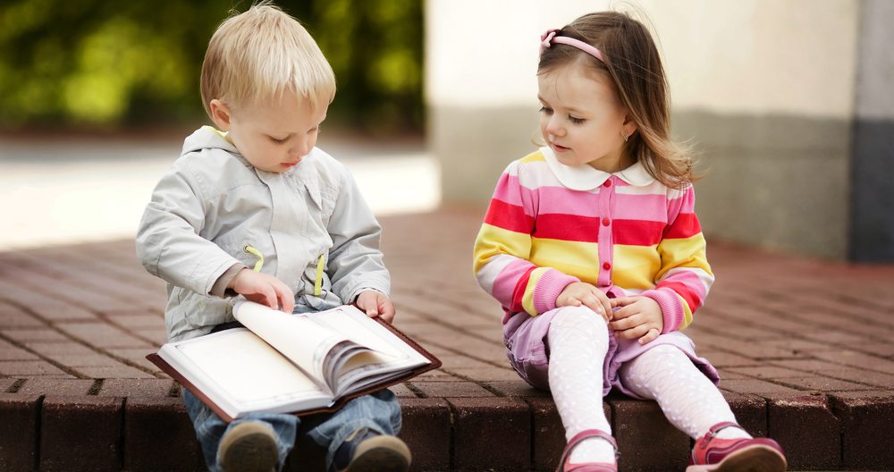 two toddlers sitting outside reading a book