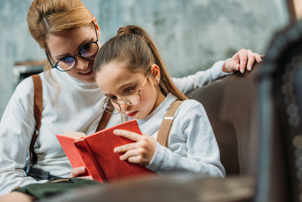 mom and daughter wearing glasses reading aloud together