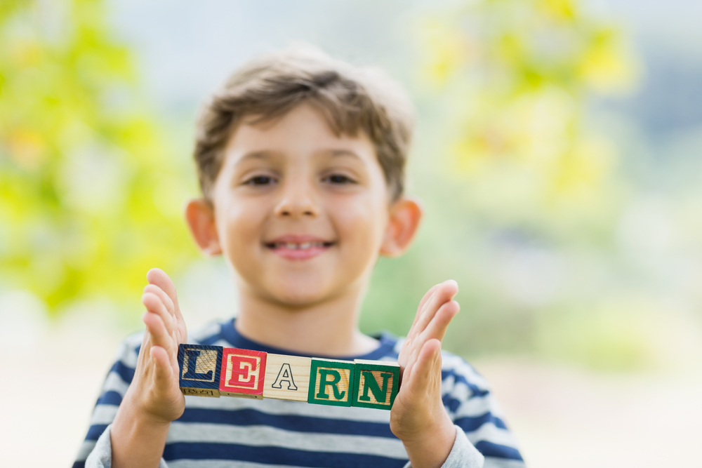 Boy holding blocks in park which reads learn