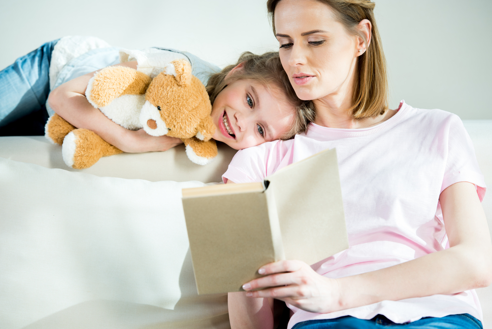 Mom reading to daughter whose holding a teddy bear