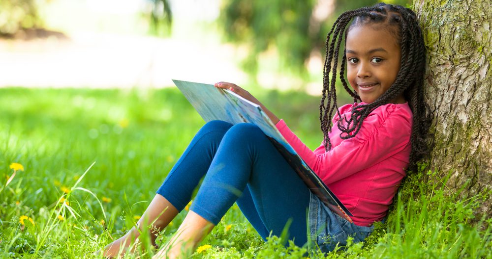 Outdoor portrait of a cute young girl reading a book