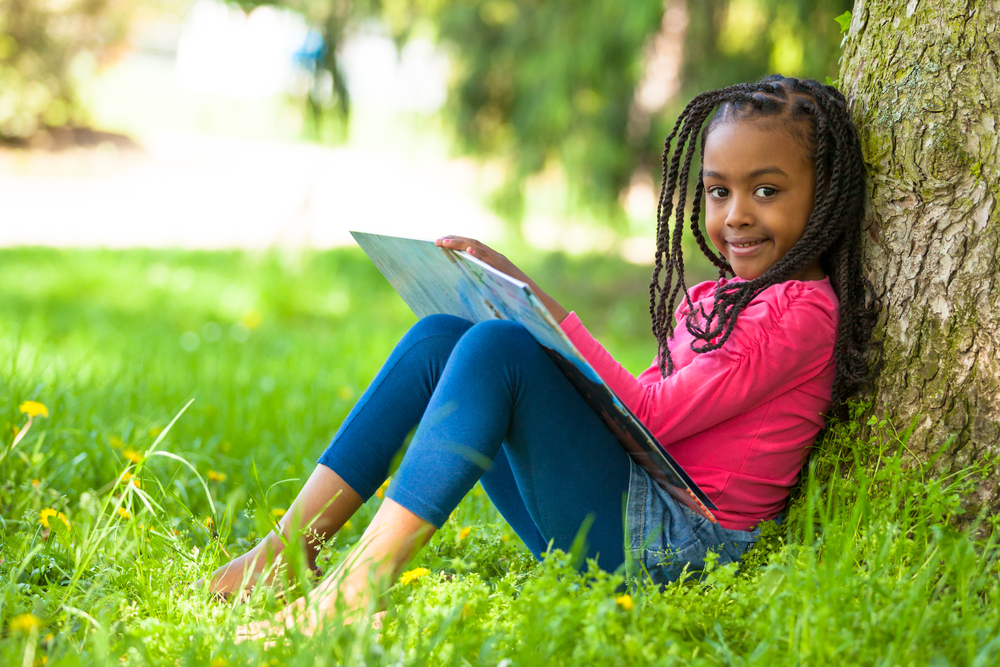 Outdoor portrait of a cute young girl reading a book