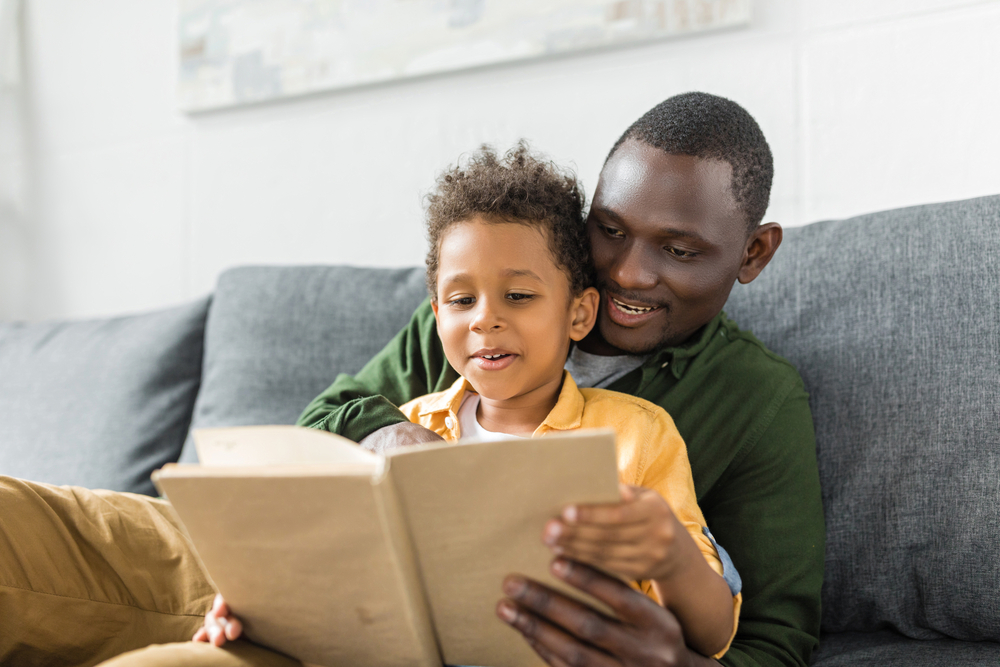 Young kid sitting with dad doing 1st-grade reading