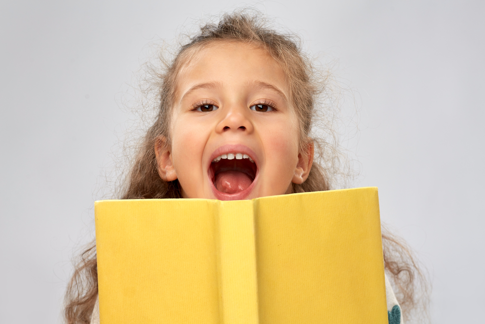 happy little girl hiding behind yellow book