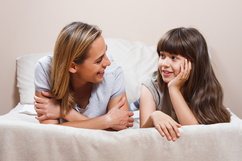 Mom talking with daughter on bed to help her express her emotions