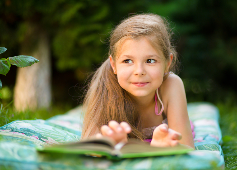 Young girl reading a book outside on a blanket