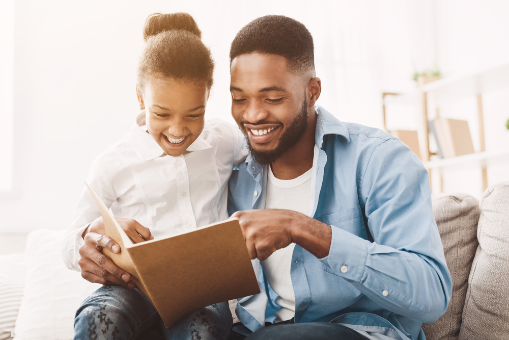 dad sitting with daughter reading a book while teaching her how to sound out words