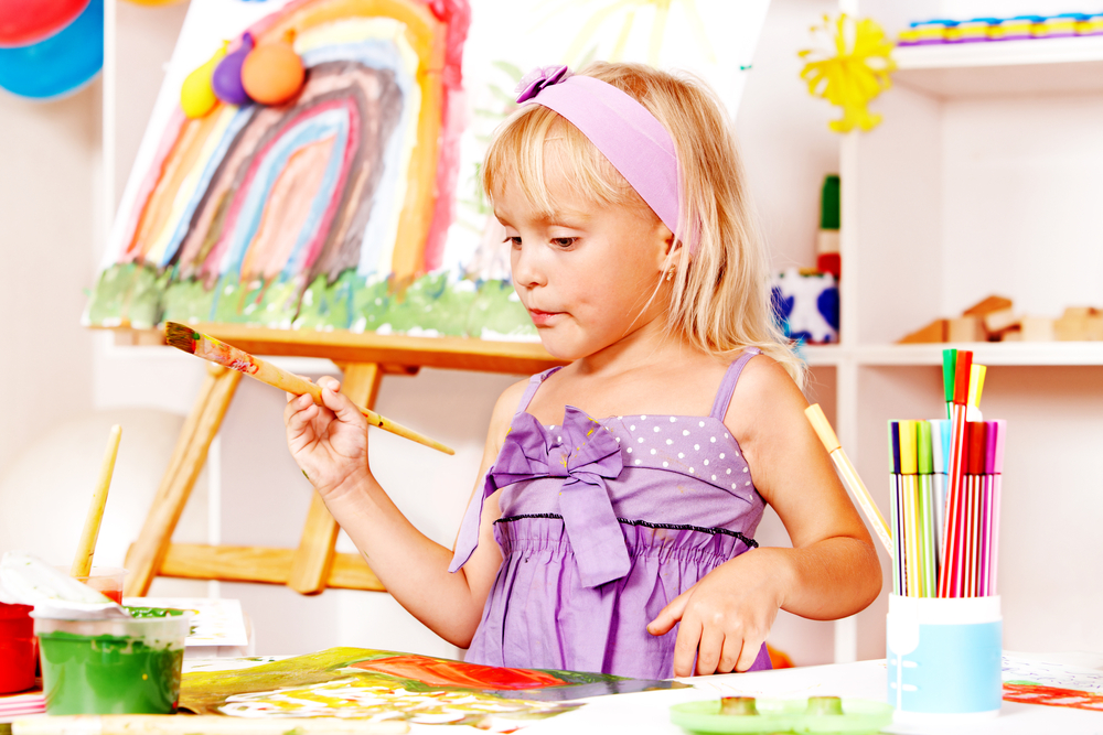 Little girl painting at easel in school.