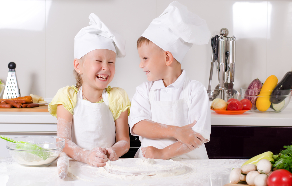 Two kids baking in bakers hats and aprons