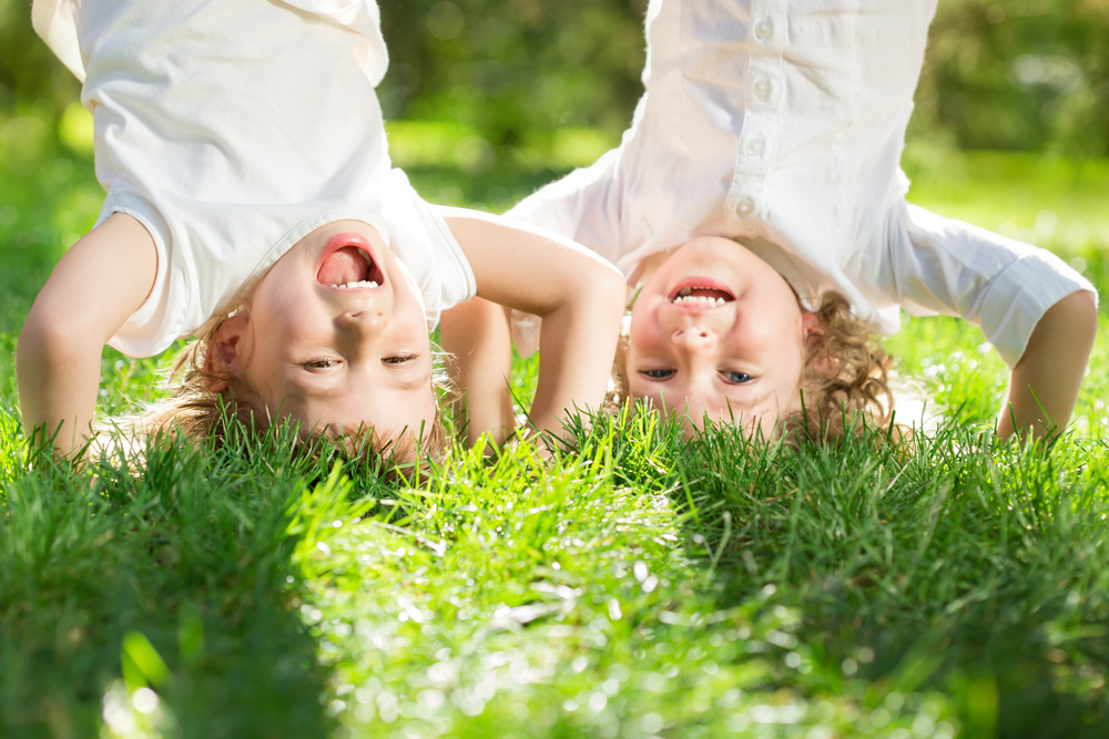 Happy children playing head over heels on green grass in spring park