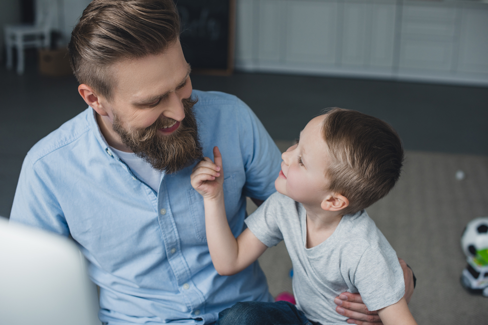 Young son looking up to dad while touching his beard
