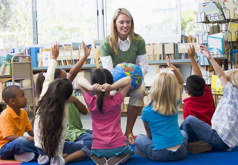 Kindergarten teacher and children with hands raised in library