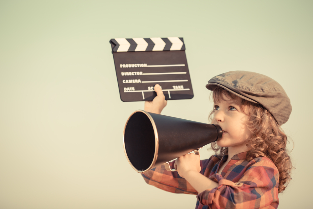 Kid holding clapper board and shouting through vintage megaphone. 