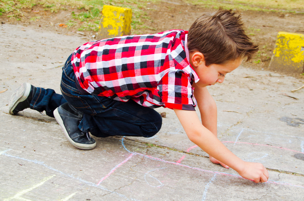 Boy drawing hopscotch with chalk on the ground
