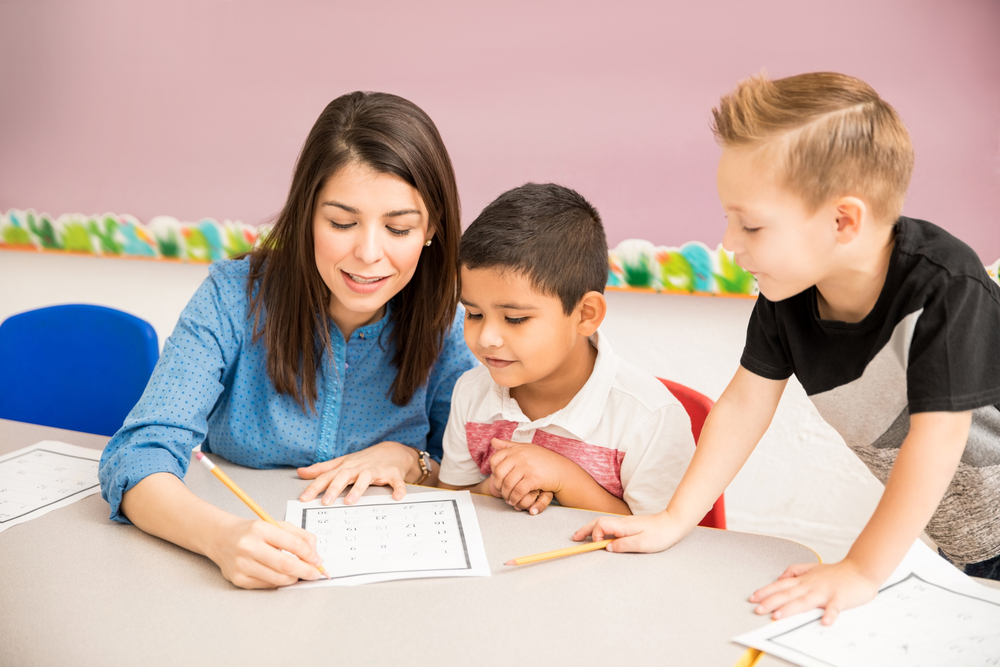 Pretty preschool teacher helping students with some math exercises in the classroom