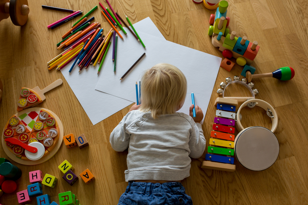 Little blonde toddler boy drawing with pastels and coloring pens