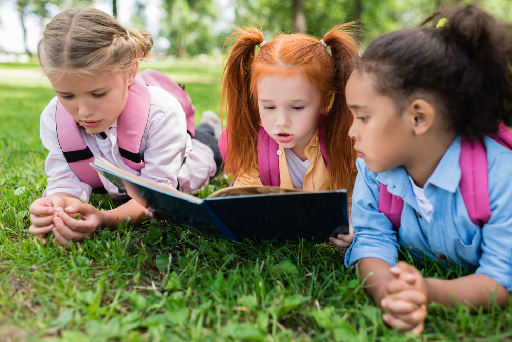 Three kids at the park reading a book together