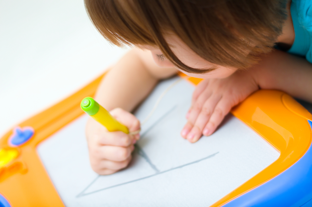 Little girl writing at magnetic drawing board