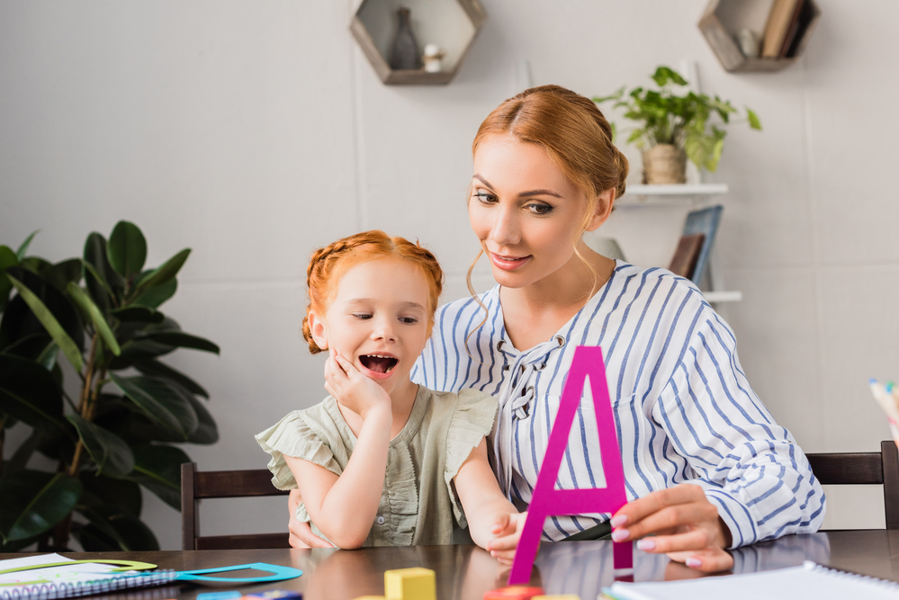 Mom using a cut out letter to teach letters to daughter