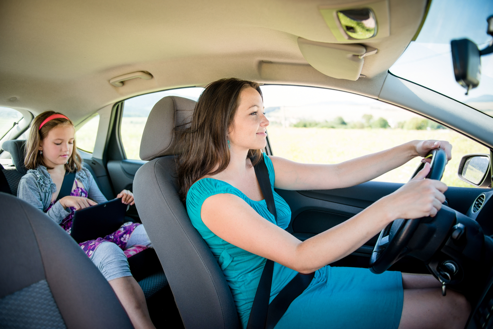 Mother driving car and child sitting on back seat and playing with tablet