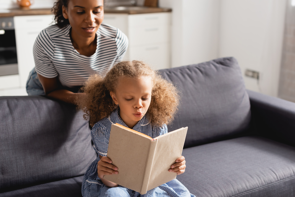 Mom helping a young girl read a book