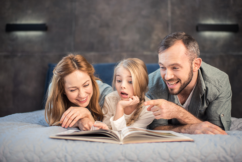 Parents teaching reading with expression to daughter
