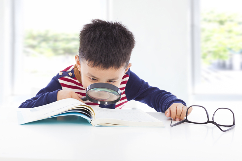 Young boy searching clues from a book with a magnifying glass