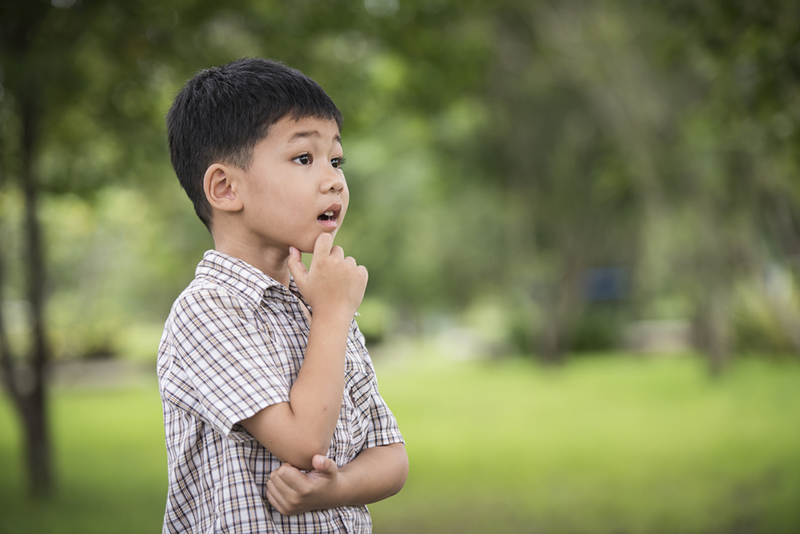 Portrait of cute boy hand under chin And Thinking While Standing over the blurred background.