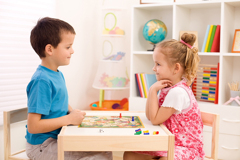 Little boy and girl playing board game in their room sitting at the table