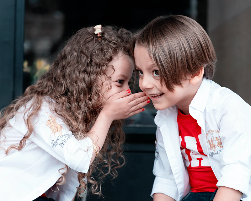 Young girl whispering to young boy
