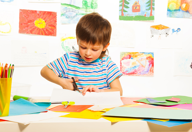 3 years old boy cutting cardboard paper with scissors in preschool art class